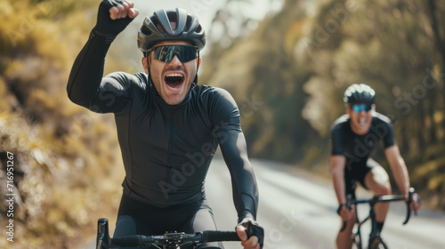 cyclist is celebrating enthusiastically with a raised fist while riding on a road, with another cyclist trailing behind
