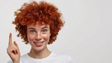 Smiling young woman with short curly red hair and cute freckles over isolated white background pointing finger to the side, with copy space.