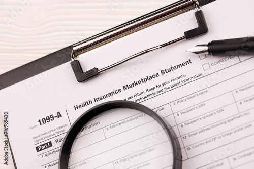 IRS Form 1095-A Health Insurance Marketplace Statement tax blank on A4 tablet lies on office table with pen and magnifying glass close up photo