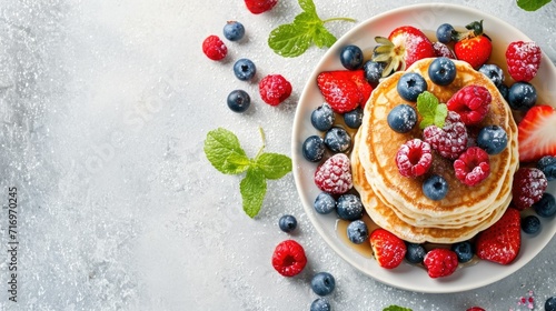 A plate of delicious pancakes topped with fresh berries and garnished with mint leaves. Perfect for a tasty breakfast or brunch option
