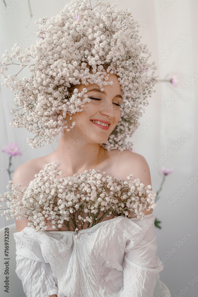 Portrait of sensual blond woman with flowers. Beautiful girl with flowers in her hair. Summer Beauty. Art in a contemporary style. A gypsophila wreath on a white background. Perfume, cosmetics concept