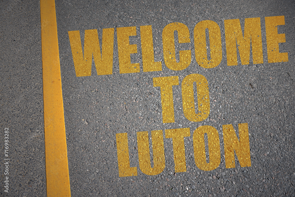 asphalt road with text welcome to Luton near yellow line.