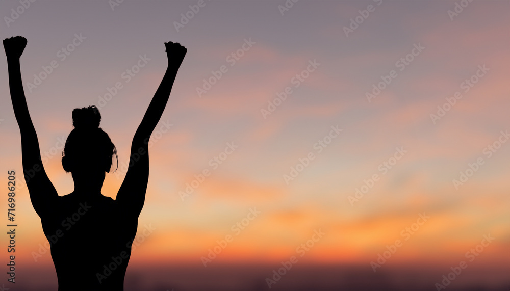 Fototapeta premium A silhouette of a woman raising her fist in the air with a sunset background