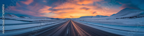 Vibrant extra wide panoramic sky. Winter highway. Snow covered street leading to te horizon. Warm fiery sunset or sunrise sky tones. Gradient shades of orange, yellow, red, pink, blue and purple. 