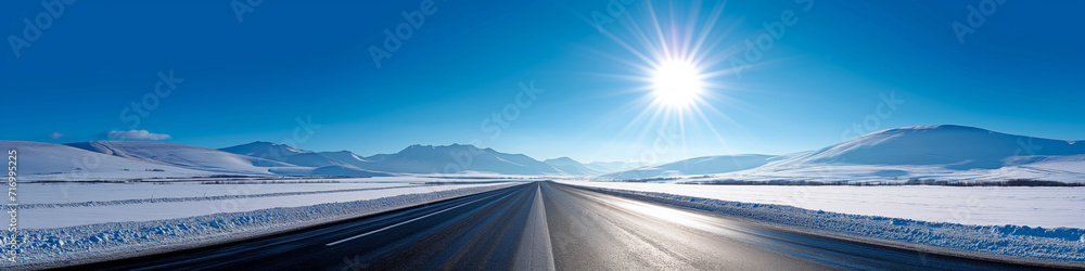 Vibrant extra wide panoramic sky. Winter highway. Snow covered street leading to the horizon. Blue sky. Fantasy winter landscape. Bright sun shining down. 