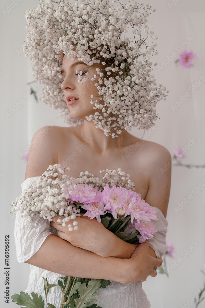 Portrait of sensual blond woman with flowers. Beautiful girl with flowers in her hair. Summer Beauty. Art in a contemporary style. A gypsophila wreath on a white background. Perfume, cosmetics concept