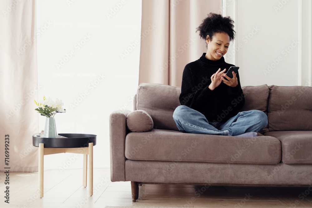 Smiling woman using smartphone comfortably at home, epitomizing relaxed technology use and modern connectivity. Smiling woman using smartphone comfortably at home, epitomizing relaxed technology use and modern connectivity.