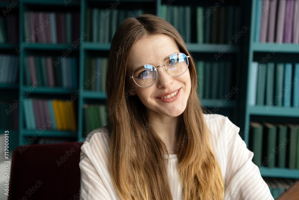 Cheerful young woman with glasses smiling in a library, surrounded by colorful books. Cheerful young woman with glasses smiling in a library, surrounded by colorful books.