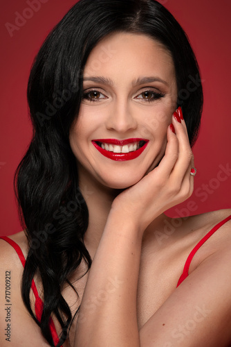 Beauty studio portrait of young beautiful smiling woman against red background.