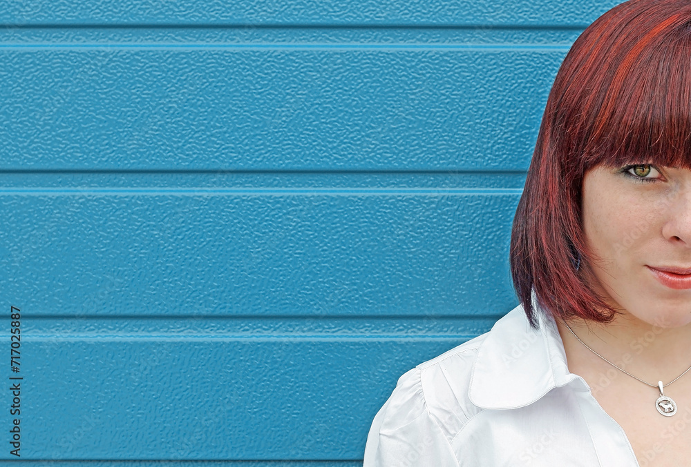 Fototapeta premium Gesichtshälfte von einer jungen rothaarigen Frau vor einem blauen Tor