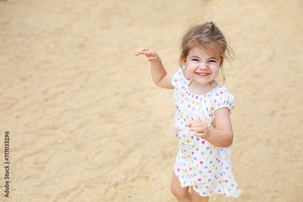 Cute blond baby girl in beautiful dress walking on a long sandy beach Cute blond baby girl in beautiful dress walking on a long sandy beach