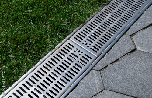 iron grate of a drainage system for storm water drainage from a pedestrian sidewalk near a green lawn.