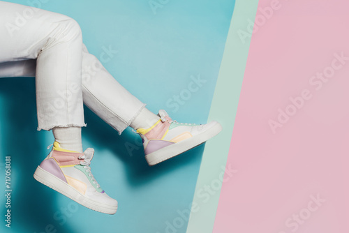 Close up female legs in white jeans and retro style high-top multicolor sport sneakers shoes on multicolor blue and pink background. Pastel candy colors, vintage retro style of 80s - 90s vibes. photo