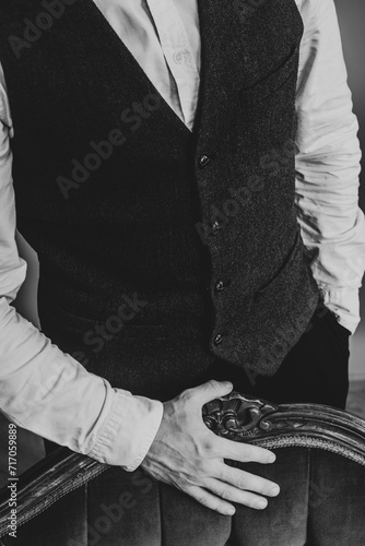 Elegant man wearing classic clothes laying his hand on a vintage couch