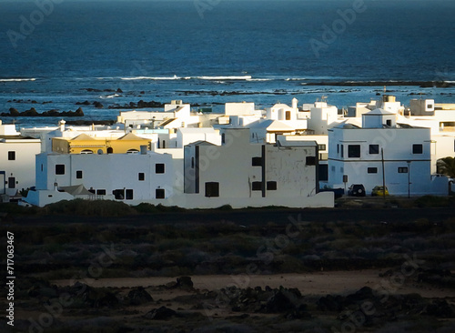 White buildings, town among volcanic black mountains and lava formations with an ocean on the background.