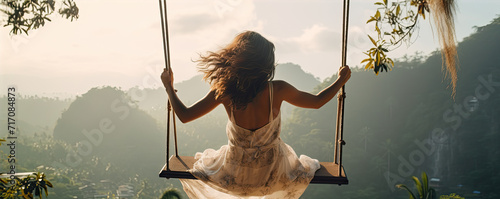 Woman swinging in sunset light. Rear view of girl swing against forest background. photo
