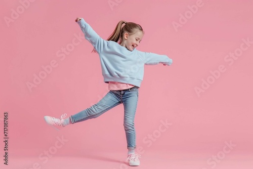 Full length photo of small girl wear stylish sweatshirt jeans raising leg up stand on tiptoe dancing isolated on pink color background photo