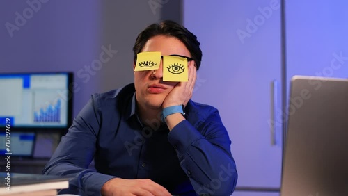 Funny lazy office worker napping at workplace covering eyes with sticky notes