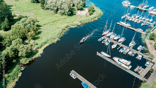 Aerial view of a peaceful marina with various sailboats docked along the pier, surrounded by lush greenery on a bright sunny day photo