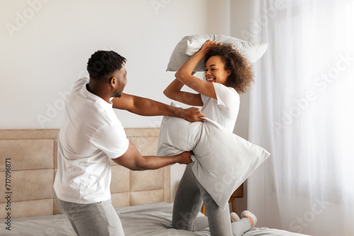 Playful loving black couple enjoys carefree pillow fight in bedroom