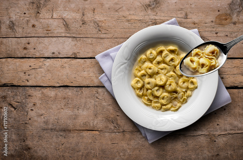 Soup plate with tortellini in broth on wooden table