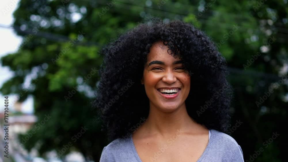 One happy Brazilian young black woman smiling and laughing while posing for camera outside in city street. Curly hair African American descent person authentic feeling joy One happy Brazilian young black woman smiling and laughing while posing for camera outside in city street. Curly hair African American descent person authentic feeling joy