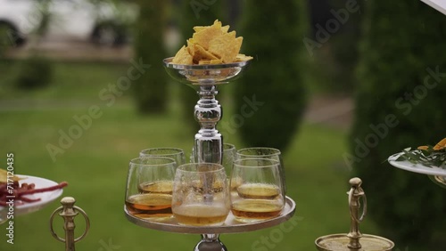 Elevate your event's ambiance with this tiered silver tray, presenting tortilla chips and whiskey on the rocks, set against a lush outdoor backdrop—perfect for lifestyle, luxury, or culinary themes