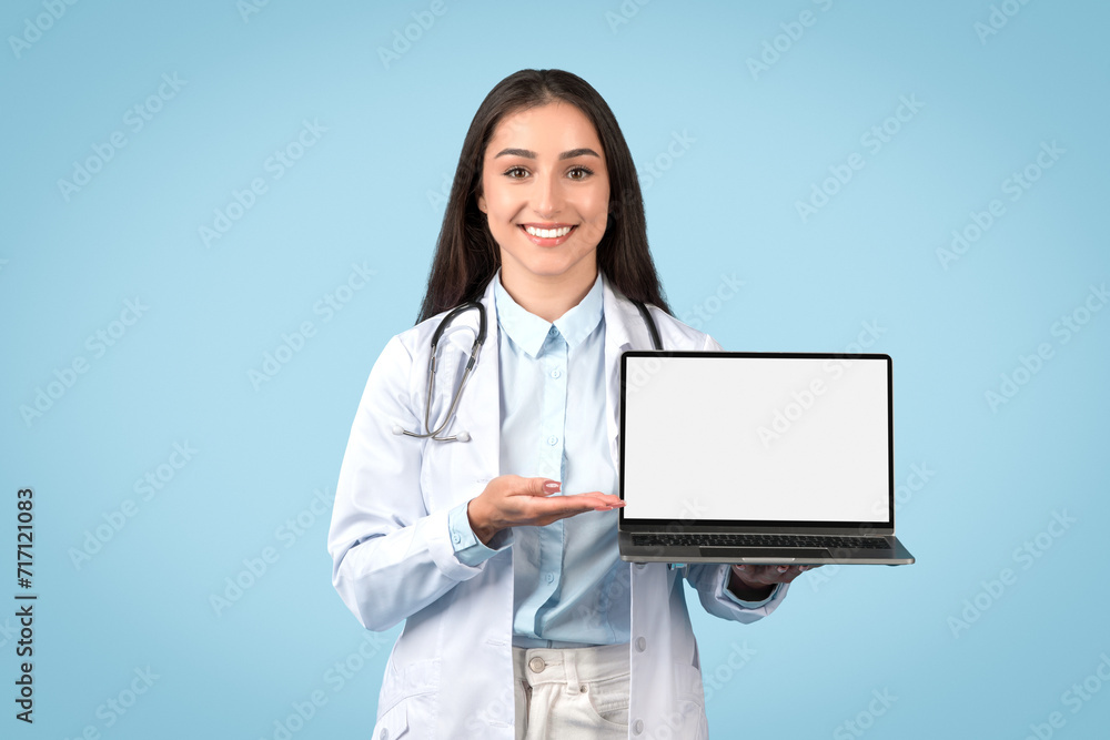 Happy woman doctor in white lab coat presenting laptop with blank screen, suitable for medical software interface Happy woman doctor in white lab coat presenting laptop with blank screen, suitable for medical software interface