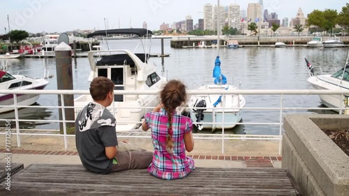 Brother and sister sitting on a bench near the moored boats photo