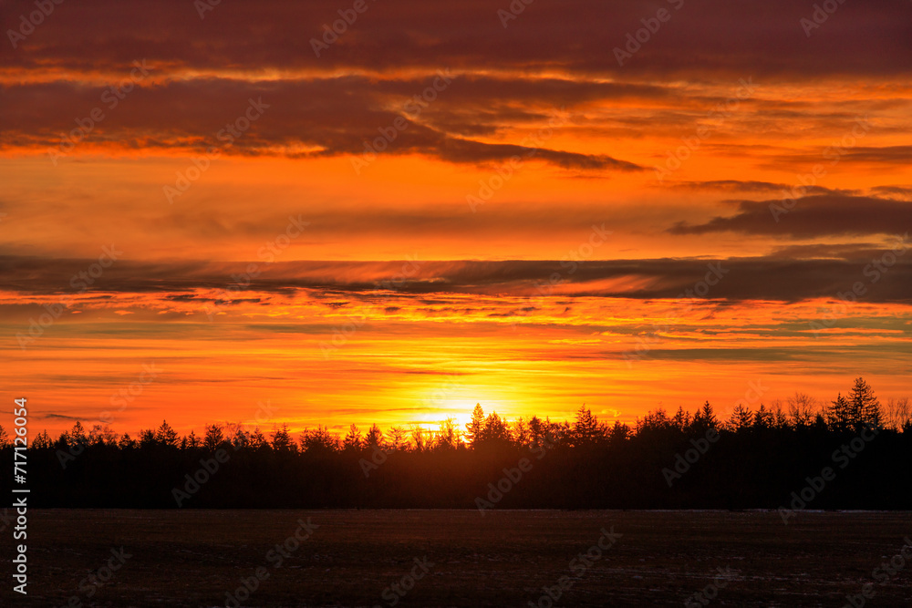 Colourful sunrise with glowing red clouds on a winter's day over the meadows and forests of Siebenbrunn, the smallest district of the Fugger city of Augsburg