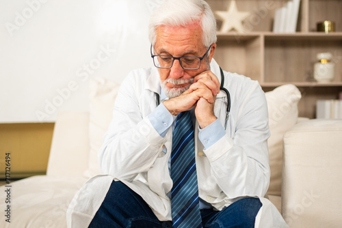 Sad tired mature senior male doctor in medical uniform in hospital or doctor office. Unhappy General Practitioner GP therapist professional healthcare expert in clinic. Healthcare concept