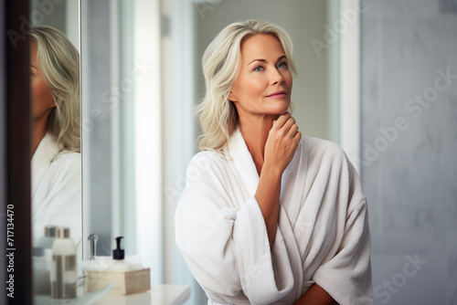 Contemplative mature woman in white robe, reflecting serenity in her bathroom.