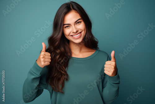 Young woman smiling with thumbs up as a sign of approval and confidence, wearing a green sweater.