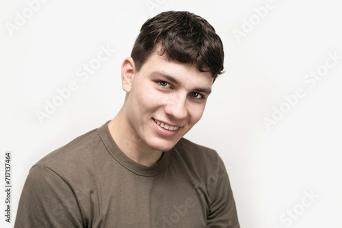 A handsome young guy is smiling sweetly, he has a nice smile and white teeth, wearing a khaki T-shirt. An athletic, brave young man is smiling on a light background © Мар'ян Філь