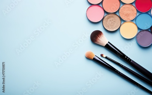 Assorted Cosmetic Powder Palettes and Makeup Brushes on a Blue Background