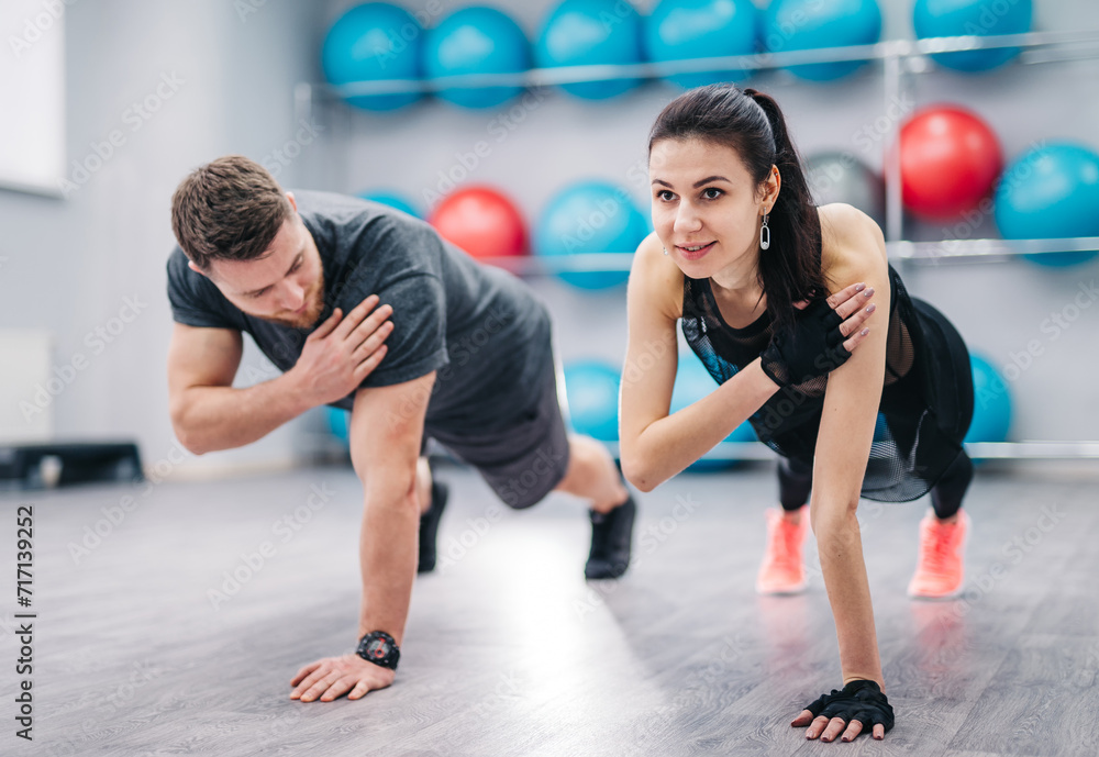 A Man and Woman Doing Push Ups in a Gym. A man and woman are positioned on the gym floor, performing push ups with precision and strength.
