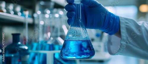 Science experiment: Analyst seals laboratory beaker containing blue liquid wearing plastic glove.