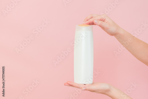 Hands holding shampoo, hair conditioner or body lotion bottle in pink background. Cosmetics bottle