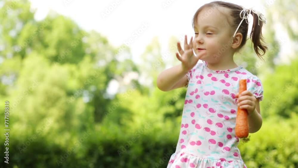 Little girl in dress eats big carrot in summer park Little girl in dress eats big carrot in summer park