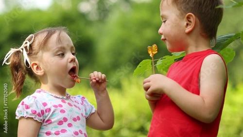 Little pretty girl and boy lick lollipops in green park photo