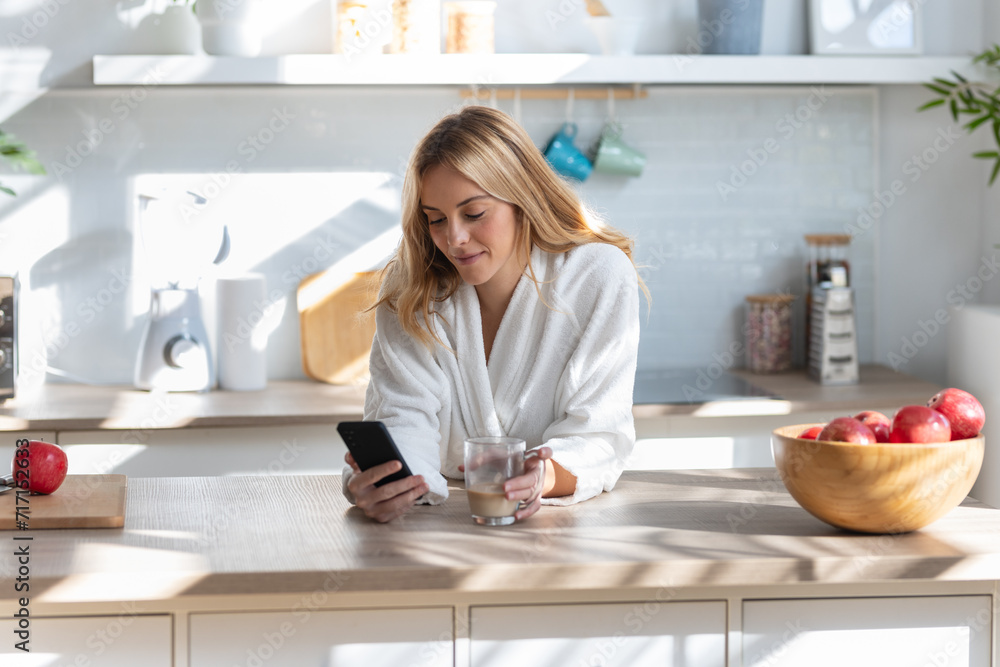 Cute young woman enjoying a cup of coffee while using her mobile phone in the living room at home. Cute young woman enjoying a cup of coffee while using her mobile phone in the living room at home.