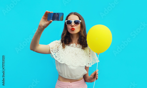 Portrait of beautiful young woman 20s taking selfie with cellphone and blowing her lips sends kiss on blue studio background