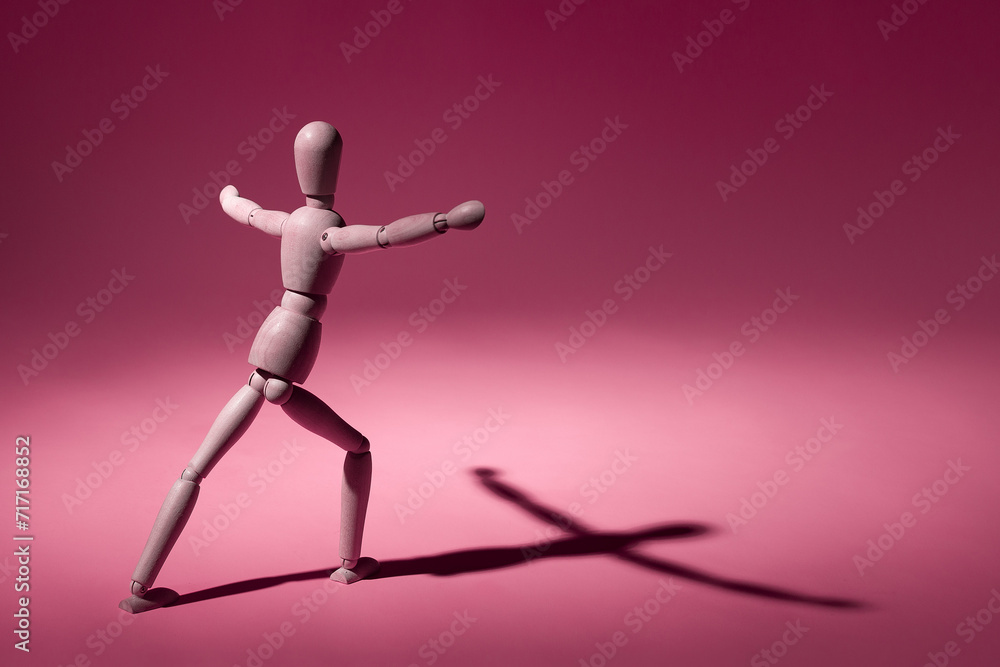 Wooden mannequin with arms outstretched in a dynamic pose, pink background, pronounced shadow.