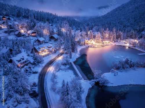 Foto Aerial view of fairy alpine village in snow, road, forest, Jasna lake, houses, street lights at winter night