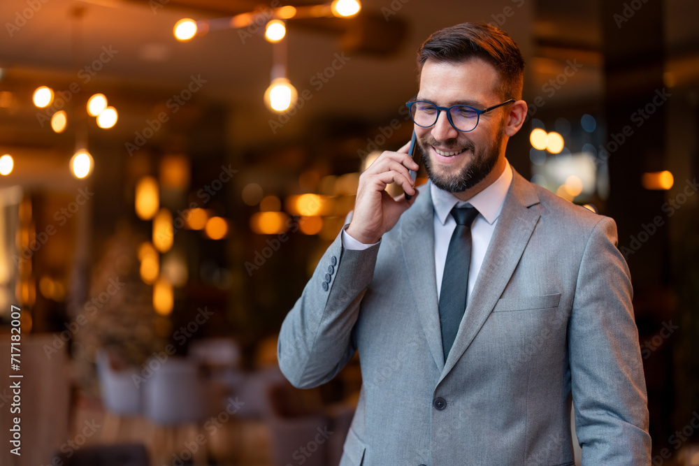 Young businessman speaking on a phone call. Happy young businessman smiling while communicating with his business partners. Successful entrepreneur working in a modern workspace. Young businessman speaking on a phone call. Happy young businessman smiling while communicating with his business partners. Successful entrepreneur working in a modern workspace.