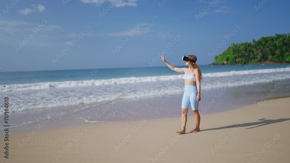 Woman in VR headset explores virtual tropics on beach, waves rolling nearby. Interactive tech adventure, touch gesture interaction, immersive experience in simulated seaside environment. Slow motion. Woman in VR headset explores virtual tropics on beach, waves rolling nearby. Interactive tech adventure, touch gesture interaction, immersive experience in simulated seaside environment. Slow motion.