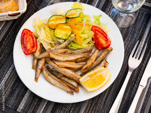 Appetizer cooked anchovies (Boquerones) with vegetable garnish on white plate. Spanish cuisine