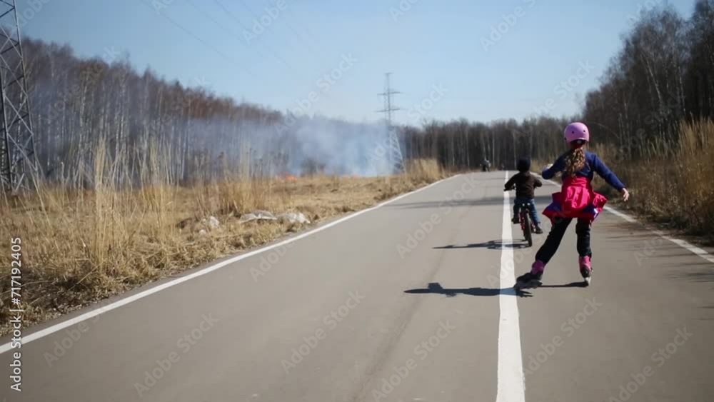 Girl on roller skates and boy on bike coming on way to burning grass Girl on roller skates and boy on bike coming on way to burning grass