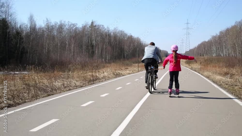 Girl riding on roller skates holding by rope to man on bicycle Girl riding on roller skates holding by rope to man on bicycle