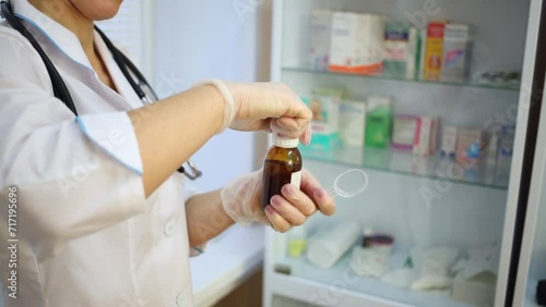 Female doctor in white lab coat opens bottle of medicine syrup. photo